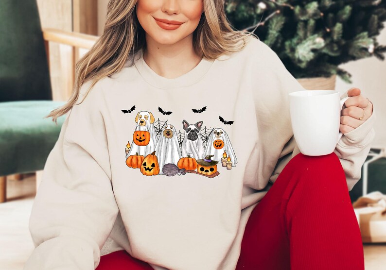 May include: A white sweatshirt with a graphic of five dogs dressed as ghosts holding pumpkins and candy. The dogs are a golden retriever, a pug, a french bulldog, a chihuahua, and a terrier. The sweatshirt is a light cream color and has a crew neck.