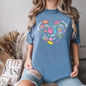 May include: A blue t-shirt with a heart-shaped design featuring various colorful illustrations of toys and the text "visual motor", "fine motor", "social", "coordination", "sensory processing", "cognition", "play", and "adis".