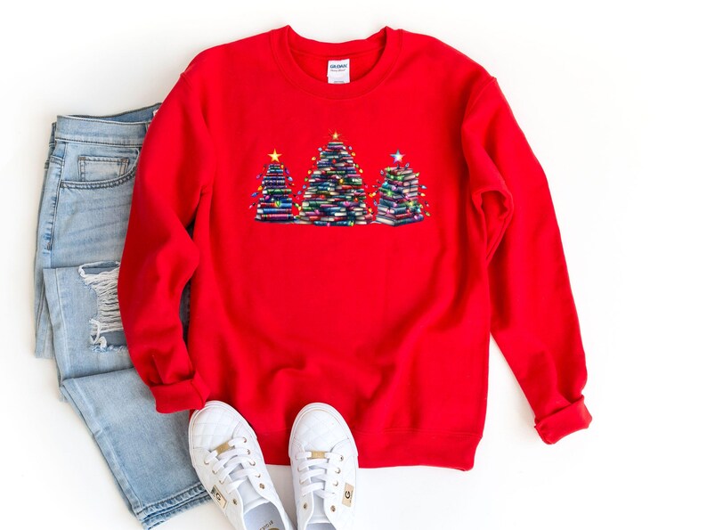 A red sweater with a Christmas tree design, a pair of blue jeans, and white sneakers are laid out on a white background.