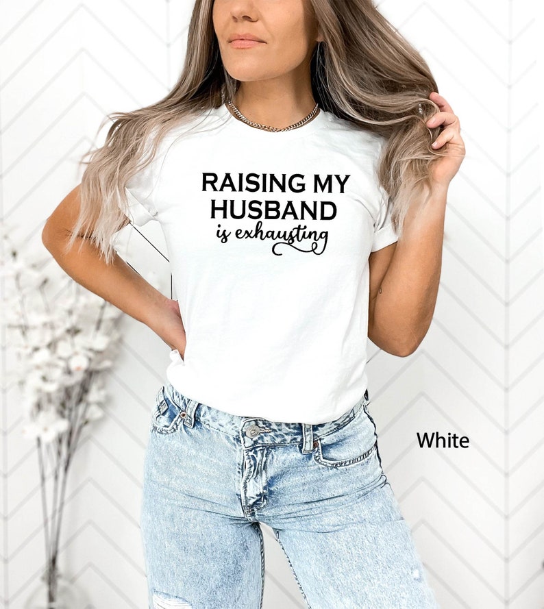 May include: White t-shirt with black text that reads "Raising my husband is exhausting".