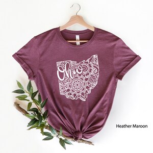 May include: A heather maroon t-shirt with a white outline of the state of Ohio. The outline is filled with a mandala design and the word "Ohio" is written inside the state.