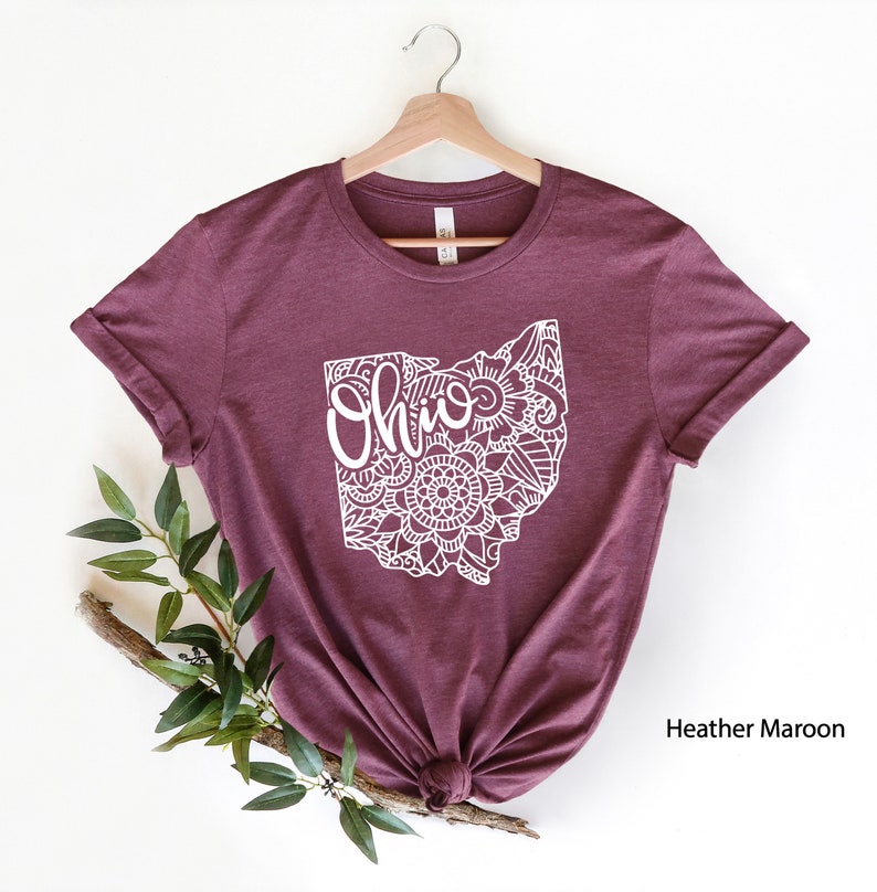 May include: A heather maroon t-shirt with a white outline of the state of Ohio. The outline is filled with a mandala design and the word "Ohio" is written inside the state.