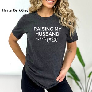 May include: A dark grey t-shirt with the text "Raising my husband is exhausting" in white.
