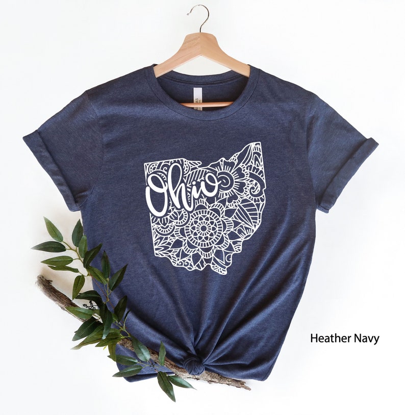 May include: A heather navy blue t-shirt with a white outline of the state of Ohio. The outline is filled with a mandala design and the word "Ohio" is written in a stylized font.