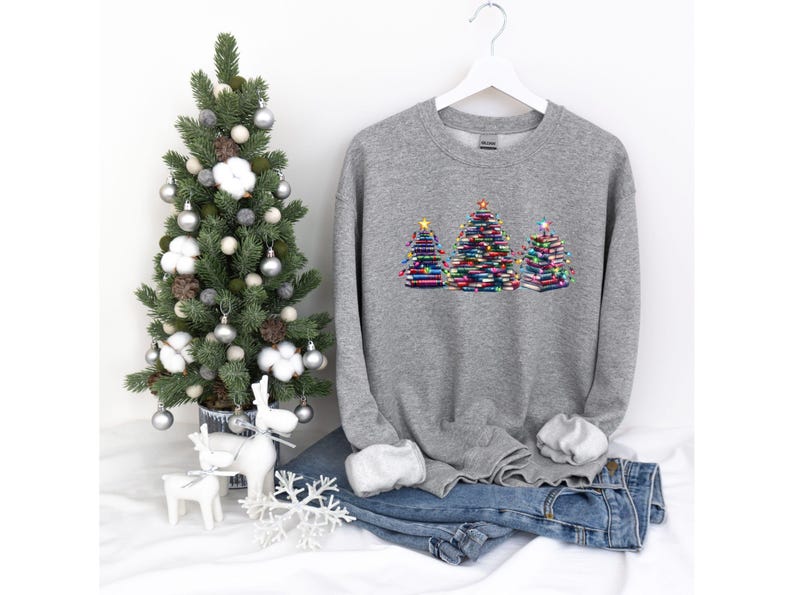 A gray sweatshirt with a Christmas tree design on it, along with a small Christmas tree, a pair of jeans, and some ornaments, all set against a white background.