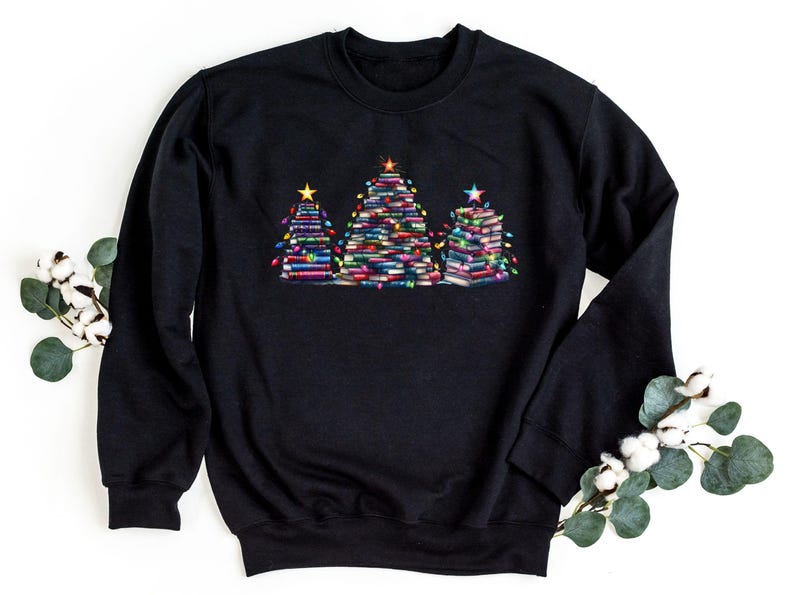 A black sweatshirt with a graphic design of three Christmas trees made of stacked books, surrounded by white cotton balls and greenery.