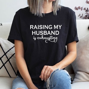 May include: Black t-shirt with the text "Raising my husband is exhausting" in white lettering.