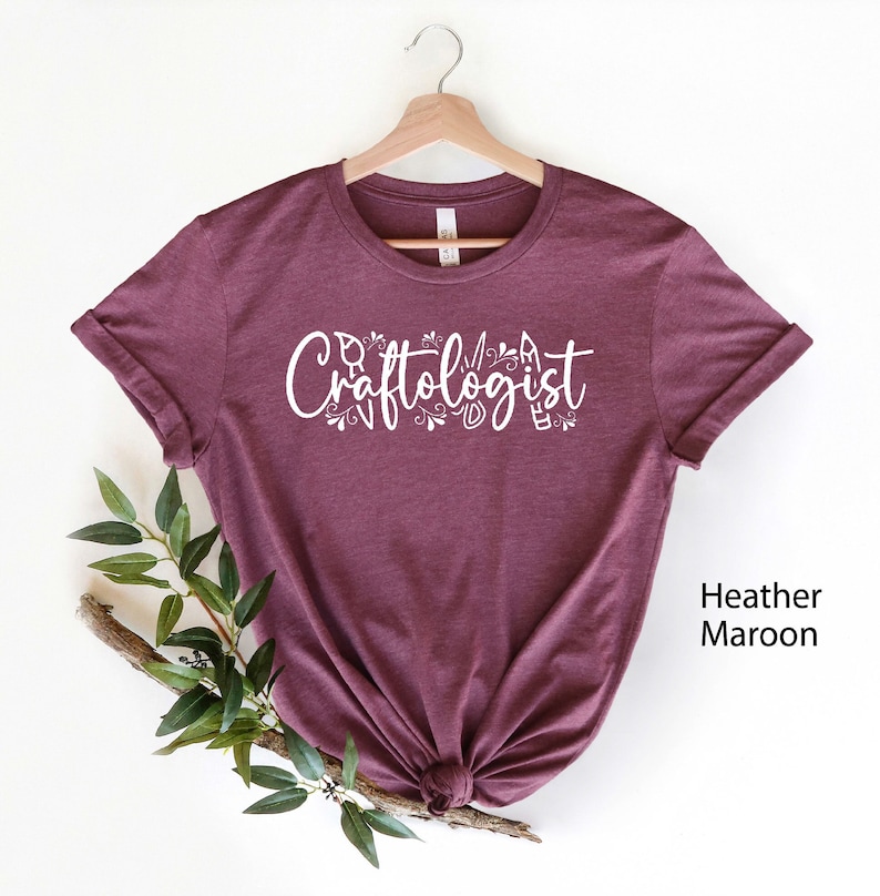 May include: A heather maroon t-shirt with the text "Craftologist" in white lettering with decorative floral accents.