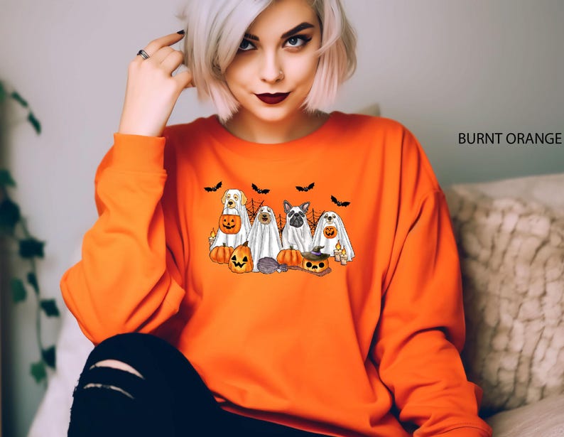 May include: Burnt orange sweatshirt with a graphic of dogs dressed as ghosts for Halloween. The dogs are holding pumpkins and wearing ghost costumes. The text "BURNT ORANGE" is in the top right corner of the image.