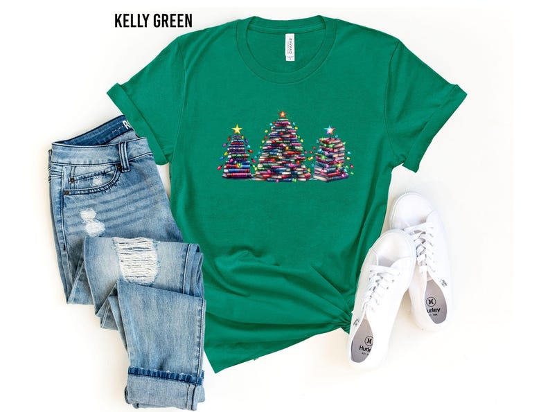 A green t-shirt with a Christmas tree design, a pair of blue jeans, and a pair of white sneakers are laid out on a white background.