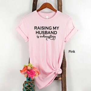 May include: Pink t-shirt with the text "Raising my husband is exhausting" in black lettering.