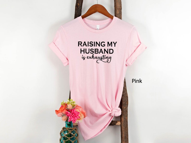 May include: Pink t-shirt with the text "Raising my husband is exhausting" in black lettering.