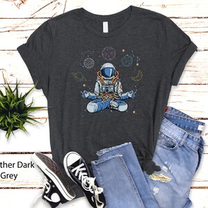 May include: Heather dark grey t-shirt featuring a meditating astronaut in space with planets and stars.