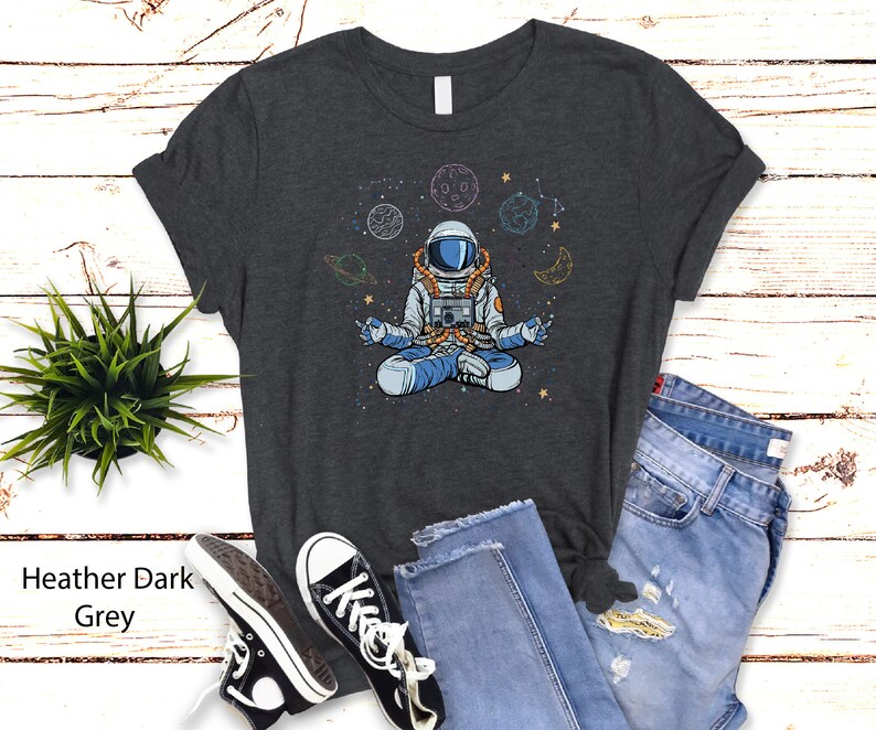 May include: Heather dark grey t-shirt featuring a meditating astronaut in space with planets and stars.