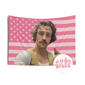 May include: Pink and white tapestry featuring a portrait of a man with a mustache, set against a pink American flag design. The tapestry includes the text "shopdilis" and a circular logo with the text "SHOP DILFS".
