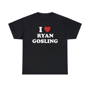 May include: Black t-shirt with the text "I ❤️ RYAN GOSLING" in white and a red heart symbol. The text is centered on the front of the shirt. The shirt has short sleeves and a crew neck.