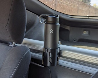 May include: A black insulated water bottle with a silver lid is secured in a black car cup holder. The cup holder is attached to the back of the front passenger seat.