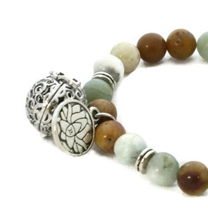 May include: A silver charm bracelet with a decorative charm featuring a lotus flower. The bracelet is made with green, brown, and white beads.