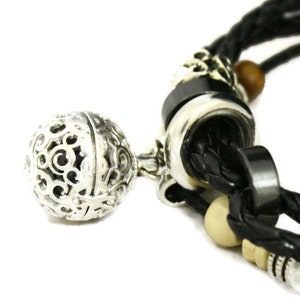 May include: A black leather bracelet with silver and black beads, a silver charm with a filigree design, and a wooden bead.