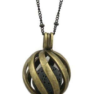 May include: A gold-toned metal cage pendant necklace with a black lava rock inside. The necklace has a black chain with small beads.