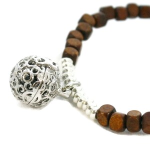 May include: A brown wooden bead bracelet with a silver charm. The charm is a sphere with a delicate, intricate design.