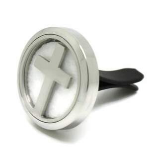 May include: Silver car air freshener with a cross design. The air freshener has a round, metal casing with a white pad inside. The air freshener is attached to a black clip.