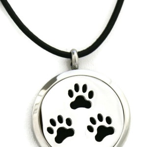 May include: A silver stainless steel aromatherapy diffuser necklace with a black leather cord. The diffuser has three paw prints cut out of the metal.