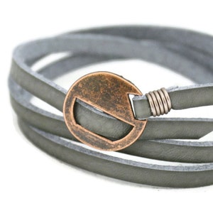 May include: A gray leather wrap bracelet with a copper-toned metal circle accent. The circle has a cut-out design.