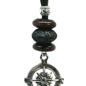 May include: A brown leather cord necklace with a compass pendant. The pendant is silver with a black compass rose and the letters N, S, E, and W. The necklace also has three beads: two brown wooden beads and one black lava rock bead.