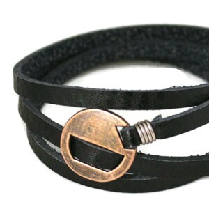 May include: A black leather wrap bracelet with a copper-toned circular clasp. The clasp has a cut-out design.