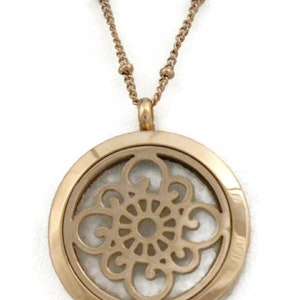 May include: A rose gold necklace with a round pendant featuring a delicate, intricate floral design. The pendant has a clear center, suggesting it may be an essential oil diffuser.