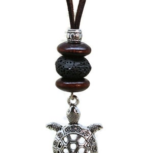 May include: A silver turtle pendant necklace with a brown leather cord. The pendant has a detailed design and is accented with brown wooden beads and a black lava rock bead.