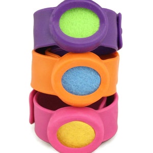 May include: Three colorful wristbands stacked on top of each other. The top band is purple with a green center, the middle band is orange with a blue center, and the bottom band is pink with a yellow center.