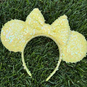 May include: Yellow sequined Minnie Mouse ears headband with a large bow on top.