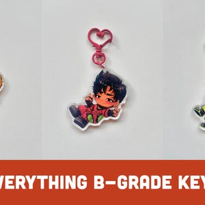 Puede incluir: Tres llaveros de personajes de estilo anime con cierres en forma de corazón. Los personajes tienen cabello naranja, negro y rojo, vistiendo atuendos coloridos. El texto "DATE EVERYTHING B-GRADE KEYCHAINS" se muestra en una pancarta roja.