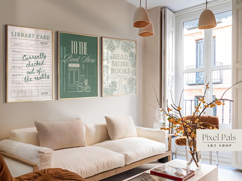 May include: Three framed art prints with book-themed quotes hang above a white sofa. The prints feature text like "Library Card," "To the Book Store," and "Read More Books." The color palette includes beige, green, and white.