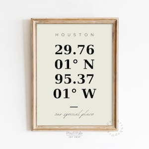 May include: A framed print with the word "HOUSTON" at the top, followed by coordinates and the phrase "our special place." The print has a light beige background and a wooden frame.