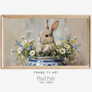 Op de afbeelding: Een ingelijste digitale kunstprint met een konijn in een blauw-witte vaas vol madeliefjes en andere wilde bloemen. Het kunstwerk heeft een zacht, pastelkleurig kleurenpalet en een vintage esthetiek. De tekst "Pixel Pals ART SHOP" staat onderaan.