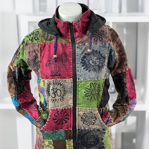 May include: A patchwork jacket with a black hood and zip. The jacket features a variety of colourful fabric squares with embroidered designs, including mushrooms, suns, and the Om symbol. The jacket has a drawstring and two pockets.