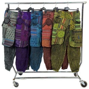 Może przedstawiać: Różne kolorowe spodnie patchwork wiszą na chromowanym wieszaku. Spodnie mają mieszankę wzorów i kolorów, w tym zielony, fioletowy, niebieski i czerwony. Każda para ma unikalny design i fakturę.