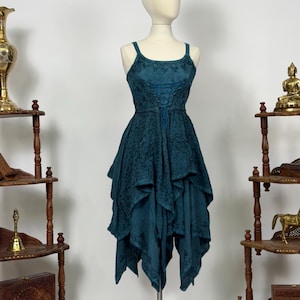 Puede incluir: Vestido color teal con corpiño estilo corsé y tirantes finos. El vestido presenta una falda asimétrica en capas y se exhibe en un maniquí. El vestido tiene un patrón floral bordado.