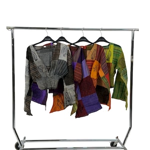 May include: Four patchwork tops in assorted colours hang on a wheeled clothes rail. The tops have a V-neck and long sleeves. Colours include grey, purple, orange, and green. Each top has a unique pattern and design.