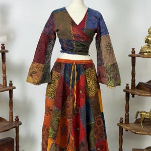 May include: A patchwork two-piece outfit comprising a wrap top and a long skirt. The top has long bell sleeves and a V-neck. The skirt has a drawstring waist. The outfit is made of various fabrics in shades of red, orange, green, and blue.