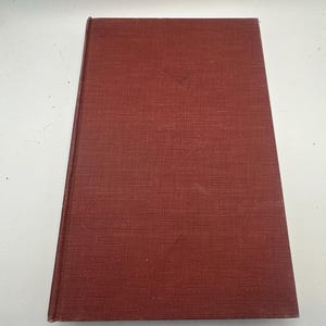 May include: A hardcover book with a textured, reddish-brown cover. The book is closed and angled slightly, showing the spine and the top edge. The cover has a subtle, woven pattern.