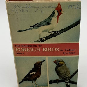 May include: The Handbook of Foreign Birds in Colour, Volume 1, by A. Rutgers. The book cover features a colorful illustration of a Gouldian Finch, a brown and white bird, and a gray and white bird.