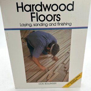 Op de afbeelding: Een boek getiteld "Hardwood Floors: Laying, sanding and finishing" door Don Bollinger. De omslag toont een foto van iemand die een houten vloer legt.