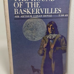 May include: The Hound of the Baskervilles book cover featuring a man in a long coat standing in front of a full moon with a wolf silhouette in the foreground. The text on the cover reads "The Hound of the Baskervilles" and "Sir Arthur Conan Doyle".