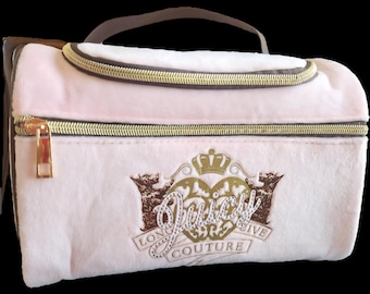 Può includere: Un beauty case rosa chiaro con cerniera dorata e manico marrone. La borsa presenta la scritta "Juicy Couture" in oro con un logo a corona e orso.