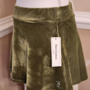 May include: A green velvet mini skirt with a Juicy Couture tag. The skirt has a small rhinestone logo on the front.