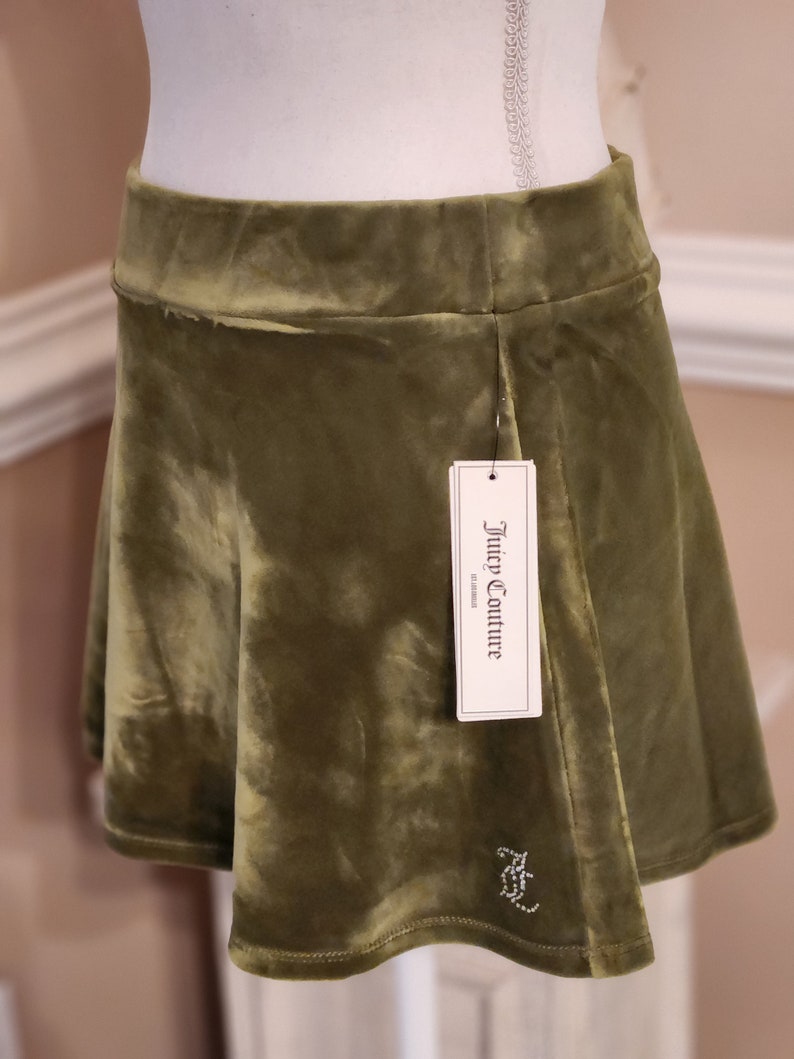 May include: A green velvet mini skirt with a Juicy Couture tag. The skirt has a small rhinestone logo on the front.